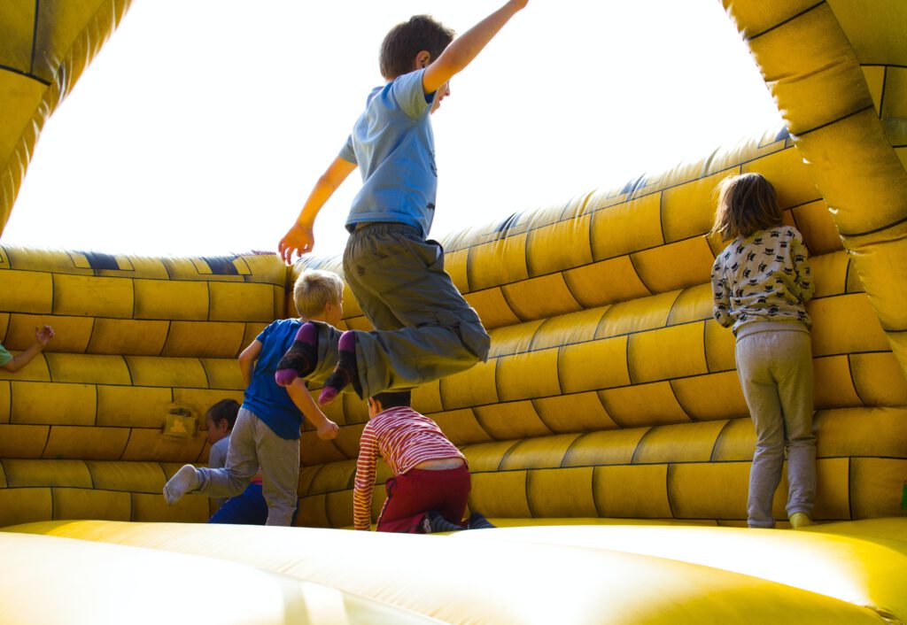 Dzieci skaczą na trampolinie w dmuchanym zamku koloru żółtego. Prezenty na Dzień Dziecka to okazja na wspólną zabawę.
