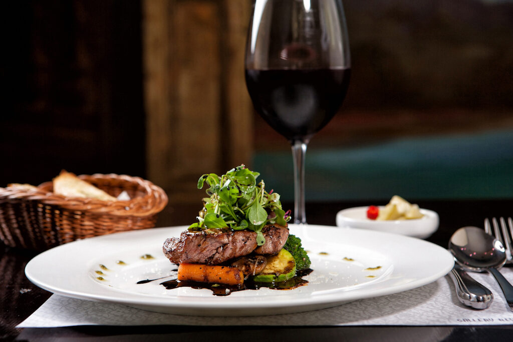 Foodpairing - talerz z wykwintynym jedzeniem, z tyłu kieliszek czerwonego wina, obok sztućce, w tle koszyk z pieczywem.