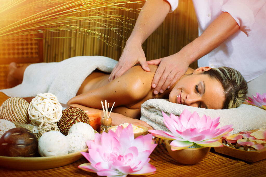 Masaż Tajski: zrelaksowana Pani jest masowana w salonie SPA, obok świeczki zapachowe i kwiatki