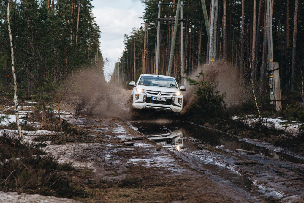 Off road- biały samochód wjeżdża w błoto i chlapie pobliskie drzewa iglaste