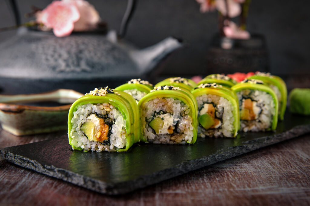Jak zrobić idealne sushi krok po kroku? Na zdjęciu rolki sushi z awokado na kamiennej płycie.