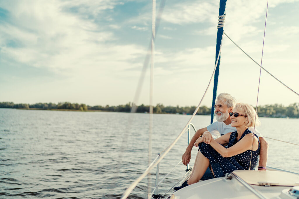 Kobieta i mężczyzna siedzą obok siebie na płynącej łodzi. W tle las i jezioro.