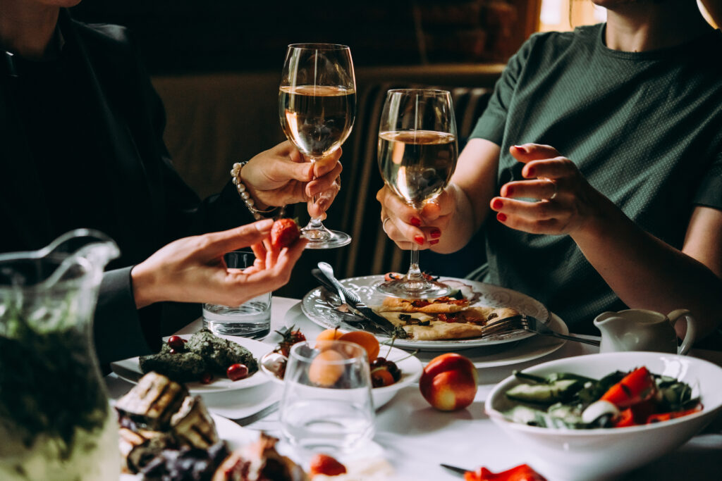 Rodzinne spotkanie w restauracji. Na stole potrawy. Ludzie unoszą kieliszki z białym winem. 