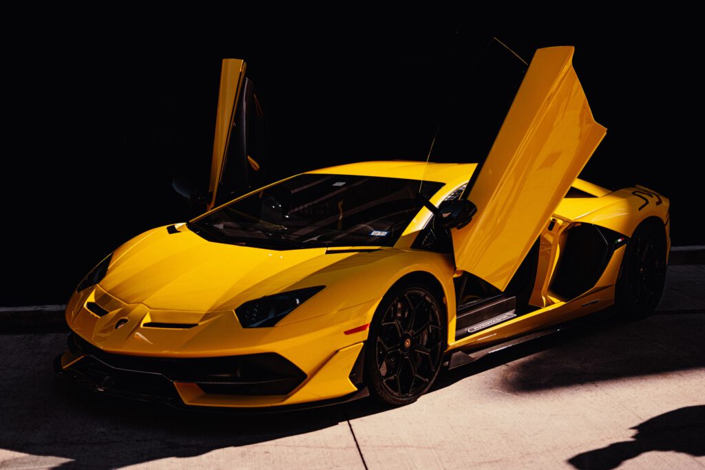 Żółte lamborghini z drzwiami otwartymi do góry stoi na podjeździe. W tle mur.