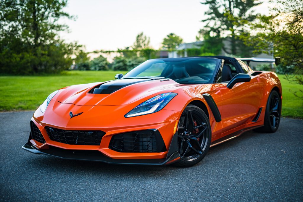 Pomarańczowe lamborghini stoi na podjeździe. W tle drzewa i dom.
