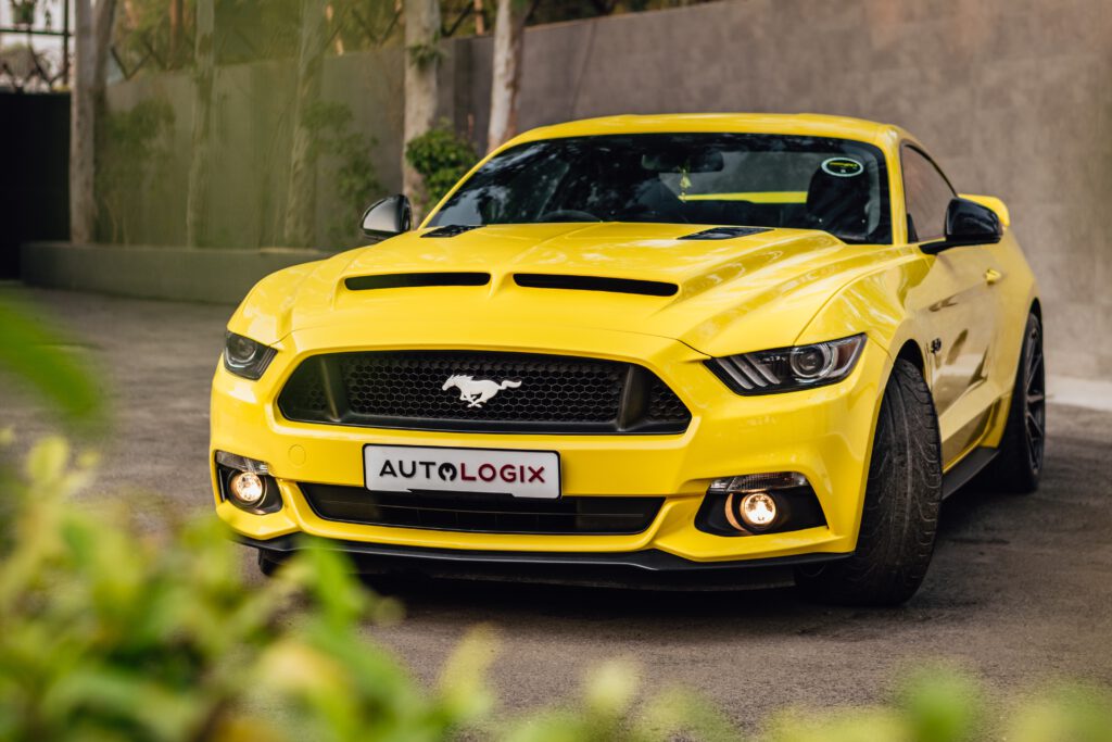 Żółty Ford Mustang stoi na drodze. W tle betonowy mur.