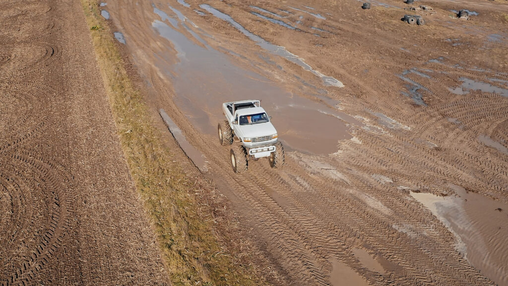 Biały Monster Truck na błotnistym torze, widok na przód pojazdu, zdjęcie zrobione dronem