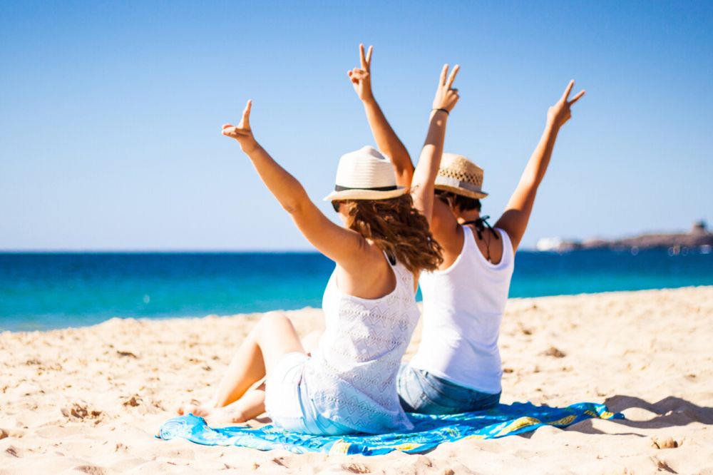 Para siedzi na plaży, z uniesionymi z radości rękami do góry