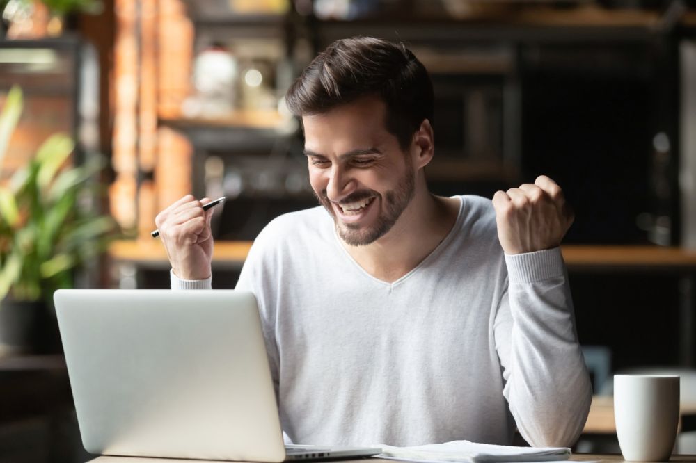 Mężczyzna cieszący się z sukcesu podczas nauki online – pozytywna reakcja przed laptopem w trakcie kursu językowego, atmosfera motywacji i satysfakcji z postępów.