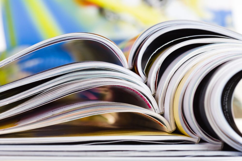 Stos otwartych kolorowych magazynów ułożonych jeden na drugim – zbliżenie na strony i grzbiety czasopism, symbol nauki, czytania i rozwijania wiedzy.